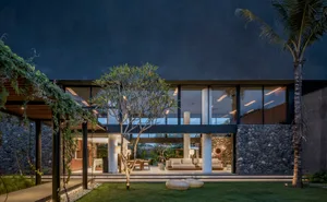 A modern house with concrete walls, glass windows, and stone accents illuminated during night time.