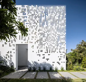 Modern building exterior featuring glass tiles with a white and gray pattern, set against a clear blue sky with landscaped gr