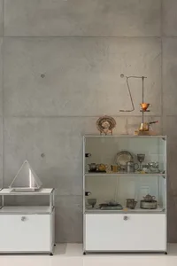 A display case featuring various metal objects, including bowls, plates, and vases, against a concrete wall.