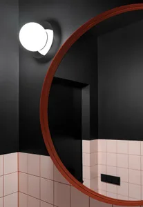 A modern bathroom with a large round mirror, black walls, and pink and white tiled floors.