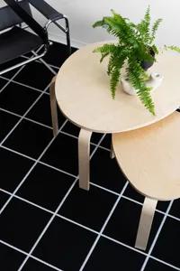 Two minimalist, round, wooden side tables stacked, with a green fern plant and a white ceramic dish on the larger table.