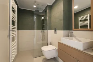 Modern bathroom with white and green tiles, white sink, and glass shower enclosure.
