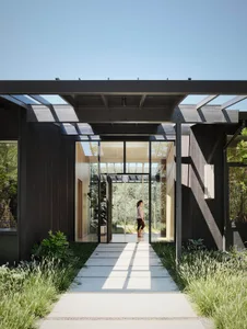 Modern house exterior with large glass windows and wooden accents, featuring a pathway and greenery.