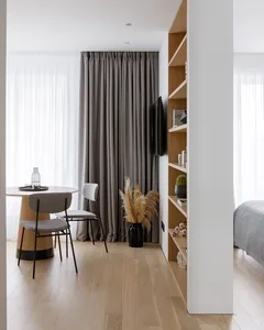 A modern minimalist residential interior featuring a dining area with a round wooden table and gray upholstered chairs, a wal