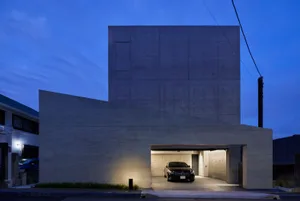 A modern residential building made of concrete at dusk with a car in the garage.