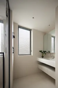 Modern minimalist bathroom with white tiled walls and floor, featuring a sleek floating vanity, frosted window blinds, and a 