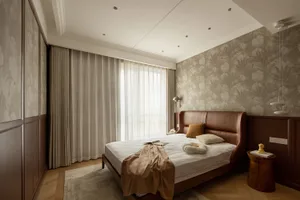 A modern bedroom featuring a leather bed, fabric bedding, and a wallpaper accent wall.
