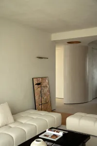 Minimalist living room with concrete walls and white furniture, featuring an abstract painting.