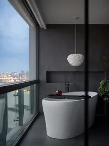 Modern bathroom featuring a freestanding bathtub made of white concrete with a red object on a tray and a white pendant lamp 