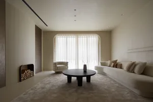 A modern minimalist living room featuring a neutral tone color palette with a curved sofa, round coffee table, and white drap