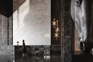 A woman standing in a luxurious industrial-style lobby with marble finishes.