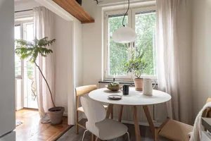 A minimalist interior with a wooden dining table, white chairs, and decorative plants by the window.