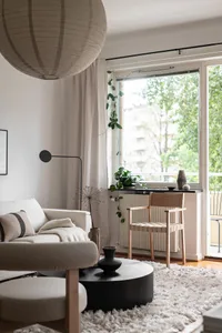 A minimalist living room featuring a couch, coffee table, and window with greenery outside.