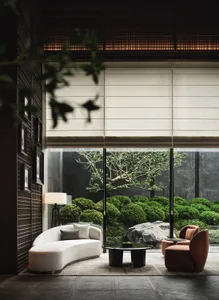 A modern living room with concrete walls, a curved white sofa, a round black table, and a view of a landscaped garden.