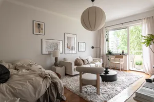 A modern minimalist living room with a white sofa, wooden chair, concrete cube, and white rug.