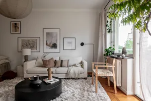 A modern, neutral-toned living room features a cozy sofa, a minimalist coffee table, and a variety of wall art.