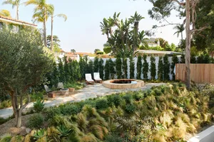 A modern garden featuring stone benches and various types of plants surrounded by white fencing and greenery.