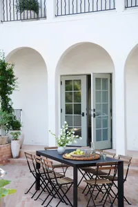 Outdoor dining area with a black metal table, wooden chairs, white flowers, and a fruit bowl.
