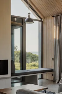 A minimalist living room with wood-paneled walls, a large window overlooking a green landscape, and a comfortable seating are