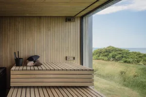 A minimalist wooden sauna with a large window overlooking the ocean.