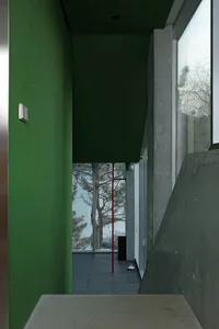A modern interior with a green wall, concrete floor, and large windows overlooking a snowy landscape.