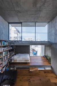 A minimalist bedroom featuring a concrete floor and wall, with a bed on a raised platform and a bookshelf.