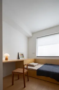 Modern minimalist bedroom with a solid wood bed, desk, and chair, featuring a large window with blinds.
