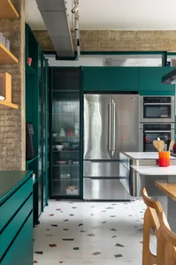 A modern industrial kitchen featuring stainless steel appliances, dark green cabinetry, and concrete flooring.