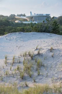 A modern house surrounded by dunes with glass walls and a white, futuristic design.