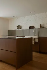 A modern minimalist kitchen with a wooden island and stainless steel countertops and sink.