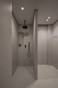 A modern bathroom with concrete walls and ceiling, featuring a black shower head and minimalist design.