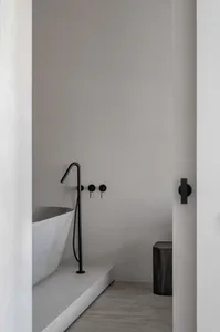 Modern, minimalist bathroom interior featuring a freestanding bathtub made of concrete with black matte hardware.