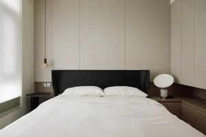 A modern minimalist bedroom featuring a white bed with black headboard, white bedding, and wooden accents.