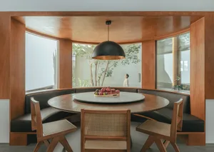 Modern dining area with round table, seating banquette, and black pendant light.