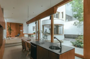 A modern kitchen featuring wood accents, black countertops, and a central island with a sink.