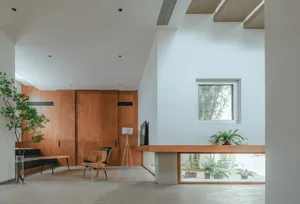 A modern living room with concrete walls and flooring, featuring a wooden chair and large window.
