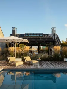Modern patio with wooden flooring and metal railings, featuring a comfortable seating area with chairs and an umbrella, overl