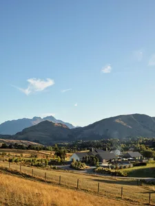 A serene rural landscape featuring a picturesque village nestled amidst mountains, with a clear blue sky above and a tranquil