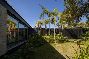 A house with a glass wall, surrounded by greenery, under a clear blue sky.
