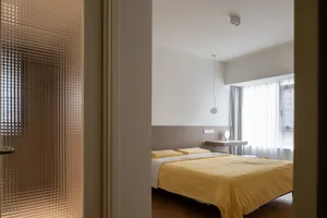 Modern minimalist bedroom with a yellow blanket and a bed, featuring clean lines and a white ceiling light.