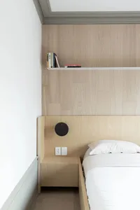 A minimalist bedroom featuring wooden furniture, white bedding, and a mounted clock.