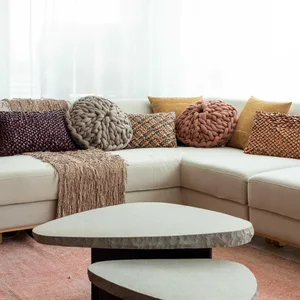 A modern living room with a white sectional sofa adorned with various textured pillows in shades of gray, brown, and yellow, 