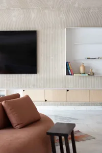 A minimalist living room featuring concrete-textured walls and a television unit with floating shelves and a bookcase below.