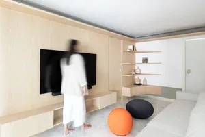 A modern living room featuring a flat-screen TV mounted on the wall, wooden paneling, and plush seating areas with orange and