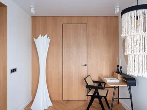 A modern home office features a wooden wall with a closed door, a sleek desk, and a minimalist white floor lamp.