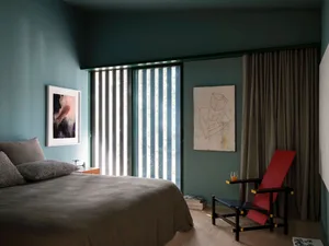 A modern bedroom featuring gray furniture, including a bed with gray bedding and pillows, and a red and black chair with a dr