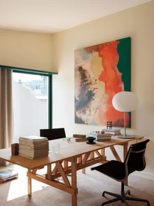 A modern workspace featuring a wooden table, chairs, and an abstract painting on the wall.