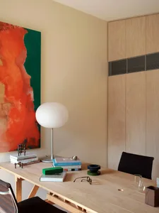 A modern office setting featuring a wooden desk with books, glasses, and a lamp, complemented by a large abstract painting on