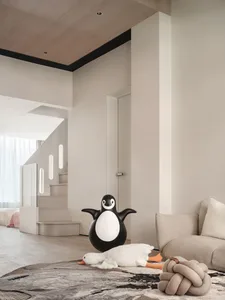 Modern living room with neutral colors, featuring a penguin-shaped floor lamp, a white duck plush toy, and a beige sofa on a 