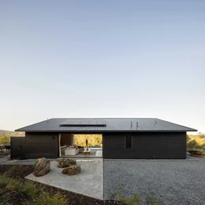 Modern minimalist house with metal roof and black exterior in a rural setting.